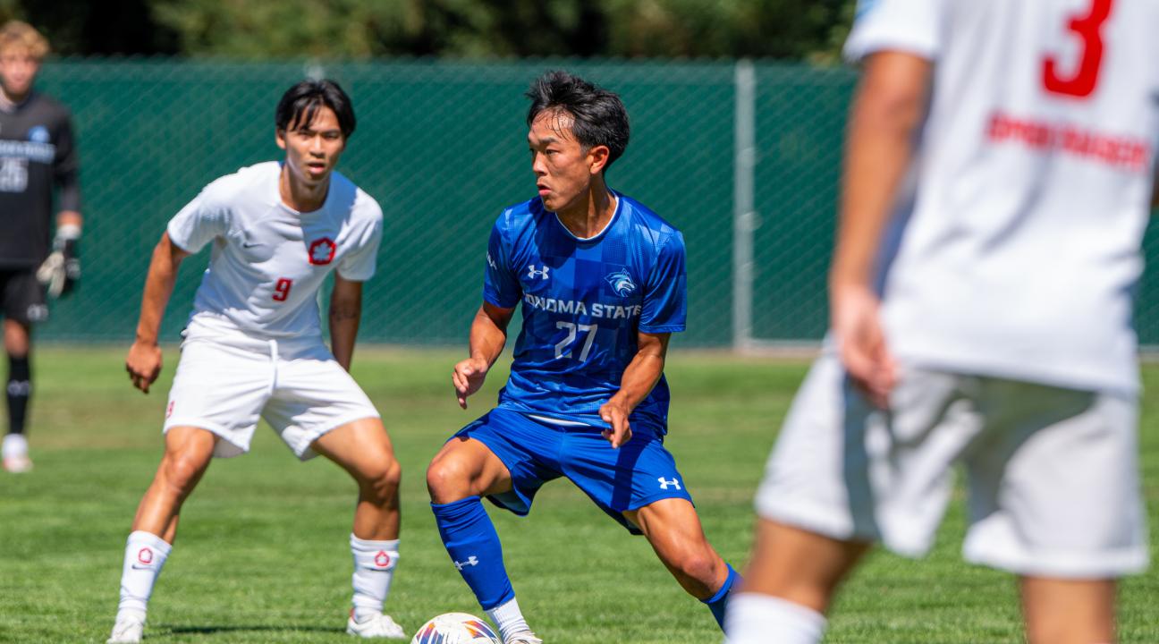 Two soccer players with one kicking a ball and one behind them as an opponent 