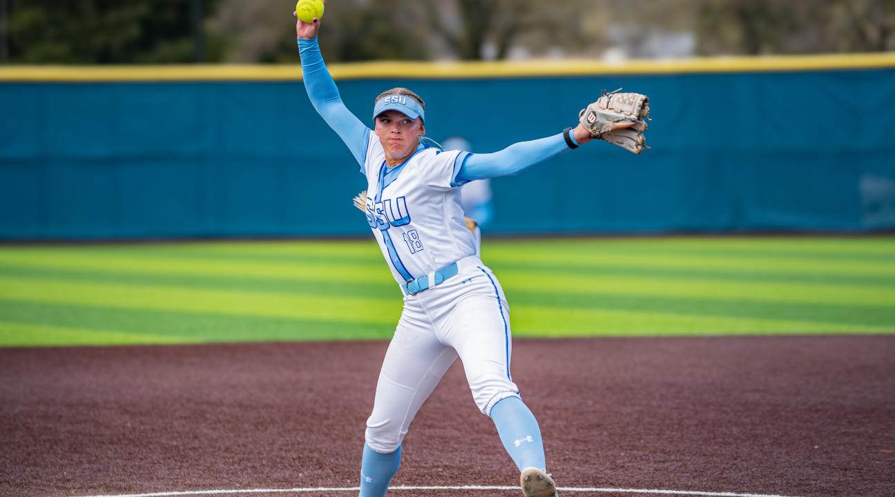 Student with a softball in one hand and glove in another throwing the ball