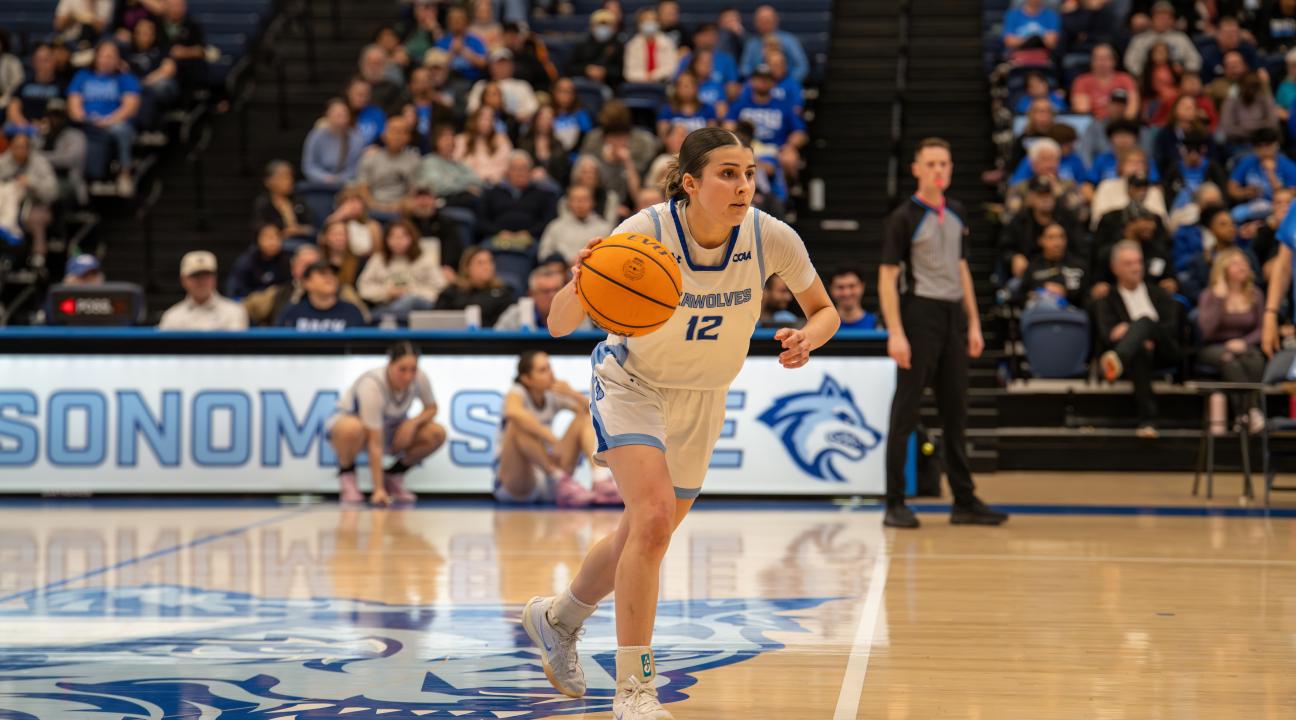 Student with a basketball in hand dribbling down a court 