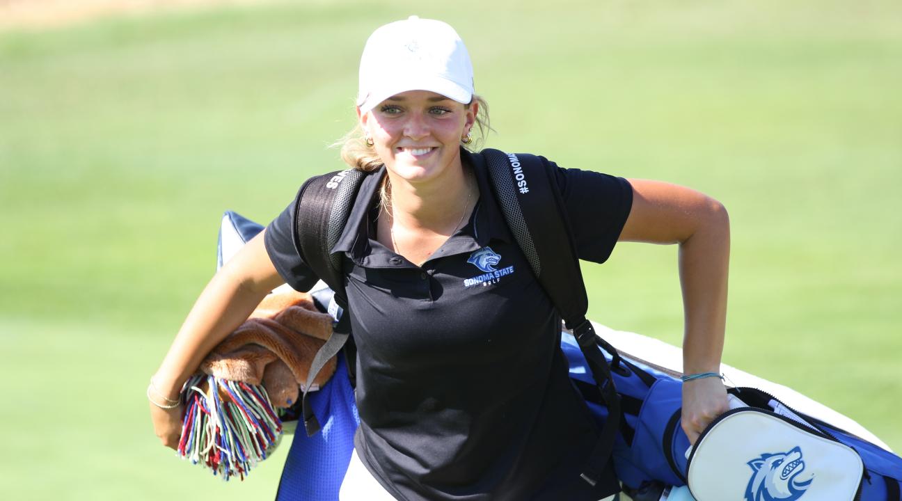 Student smiling and holding a golf bag with clubs