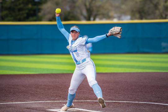 Student with a softball in one hand and glove in another throwing the ball