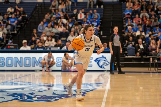 Student with a basketball in hand dribbling down a court 