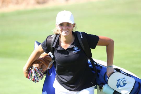 Student smiling and holding a golf bag with clubs